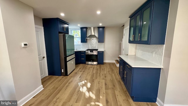 kitchen featuring blue cabinetry, stainless steel appliances, wall chimney range hood, light hardwood / wood-style flooring, and decorative backsplash