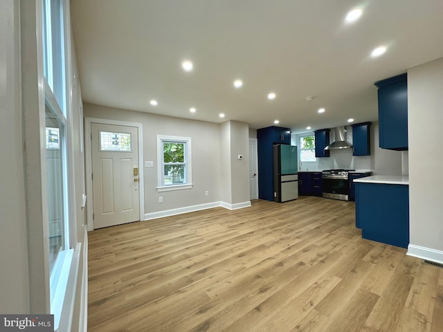 kitchen featuring wall chimney exhaust hood, light wood-type flooring, blue cabinets, and appliances with stainless steel finishes