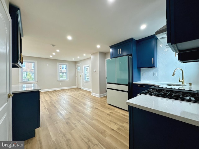 kitchen with blue cabinetry, light stone countertops, sink, light hardwood / wood-style flooring, and fridge