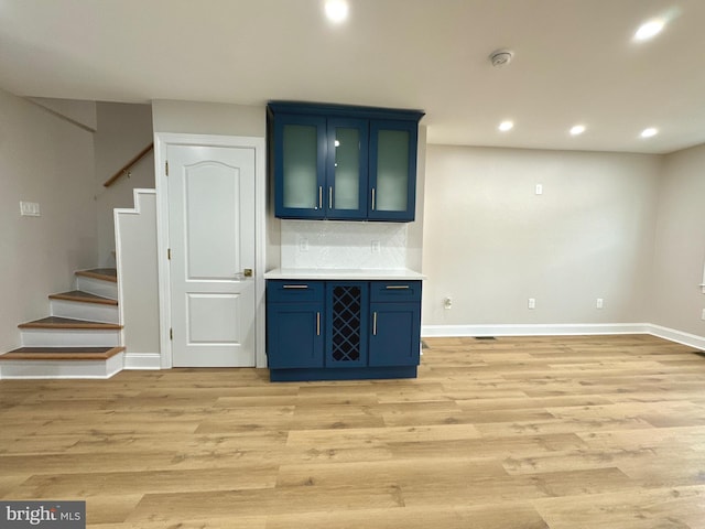 bar with decorative backsplash, light hardwood / wood-style floors, and blue cabinetry