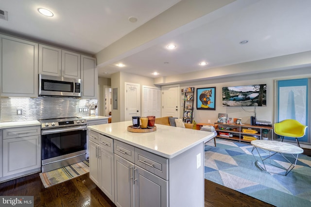 kitchen featuring tasteful backsplash, appliances with stainless steel finishes, dark hardwood / wood-style floors, gray cabinets, and a center island