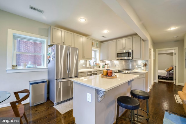 kitchen with a breakfast bar area, stainless steel appliances, a center island, dark hardwood / wood-style flooring, and tasteful backsplash