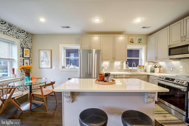 kitchen featuring a kitchen island, dark wood-type flooring, backsplash, sink, and appliances with stainless steel finishes