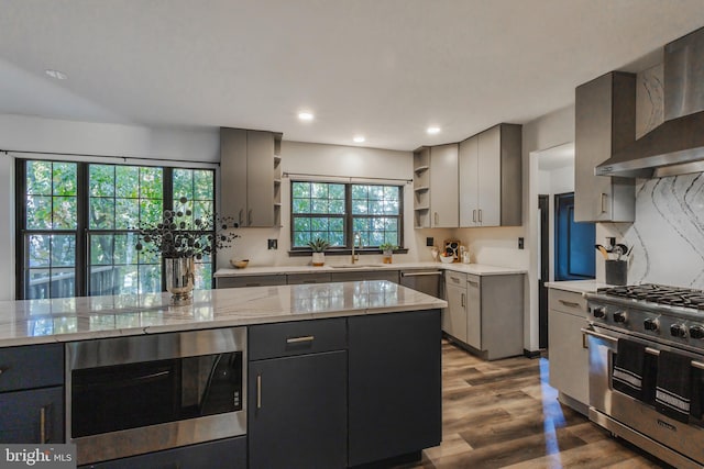 kitchen featuring wall chimney range hood, light hardwood / wood-style flooring, sink, appliances with stainless steel finishes, and light stone counters