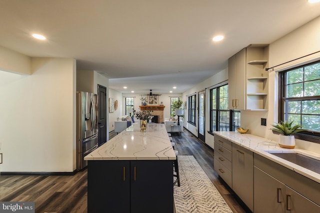 kitchen featuring light stone counters, a kitchen island, stainless steel refrigerator with ice dispenser, and dark wood-type flooring