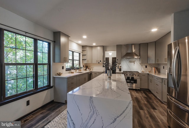 kitchen featuring wall chimney range hood, light stone counters, dark hardwood / wood-style flooring, stainless steel appliances, and a center island