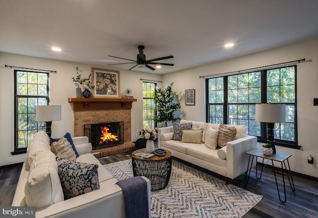 living room featuring ceiling fan, dark wood-type flooring, plenty of natural light, and a brick fireplace