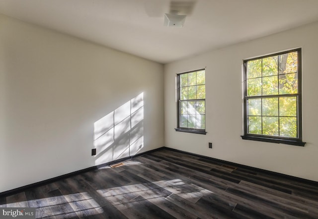 empty room with dark hardwood / wood-style floors and plenty of natural light