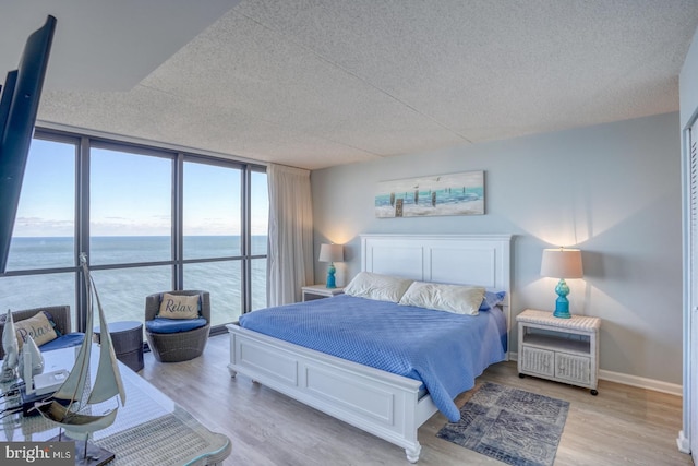 bedroom with expansive windows, light hardwood / wood-style flooring, a water view, and a textured ceiling