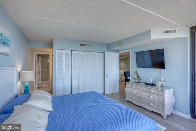 bedroom with a closet, ensuite bathroom, light hardwood / wood-style flooring, and a textured ceiling