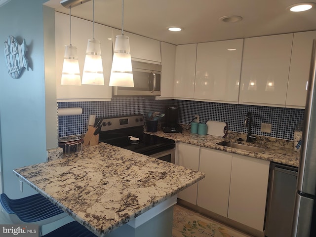 kitchen with kitchen peninsula, appliances with stainless steel finishes, sink, white cabinets, and hanging light fixtures