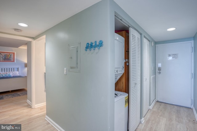 hall featuring stacked washer / dryer, electric panel, and light hardwood / wood-style flooring