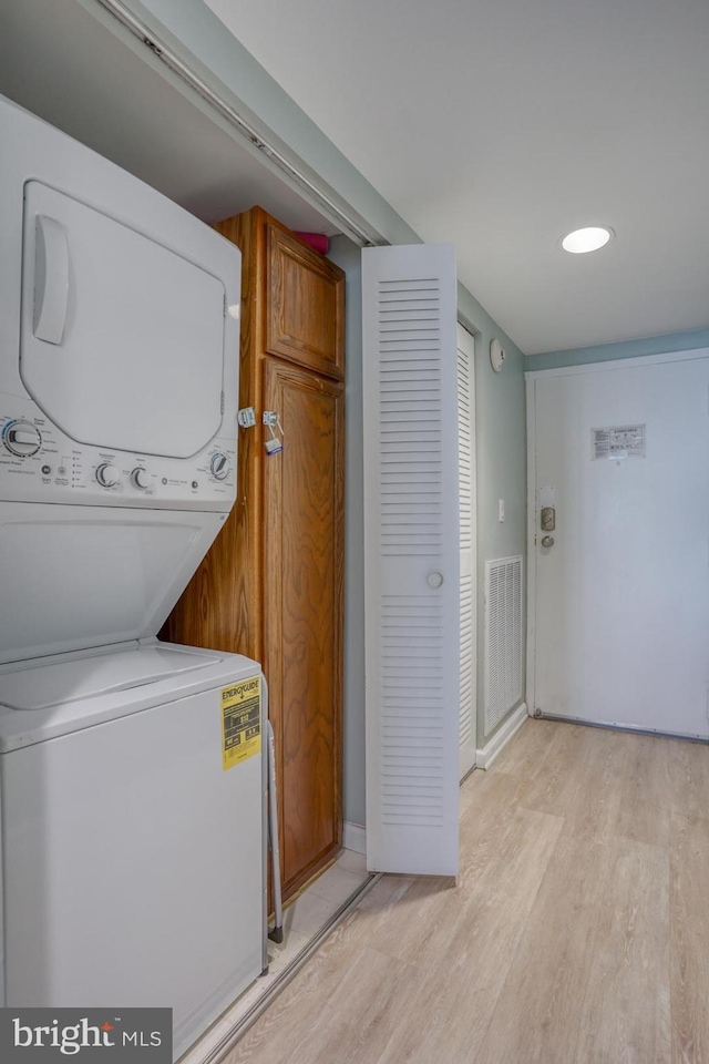 laundry room with stacked washer and dryer and light hardwood / wood-style flooring