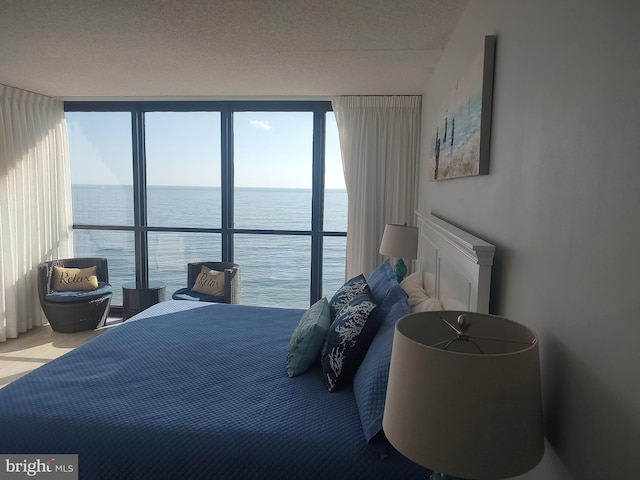 bedroom featuring a textured ceiling, a water view, and floor to ceiling windows