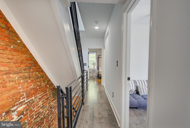 hallway with brick wall and hardwood / wood-style floors