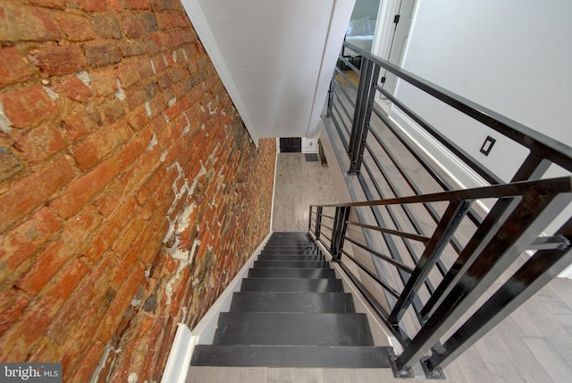 stairs with hardwood / wood-style flooring and brick wall