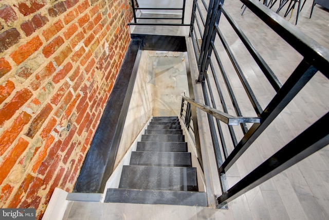 stairway with brick wall and wood-type flooring