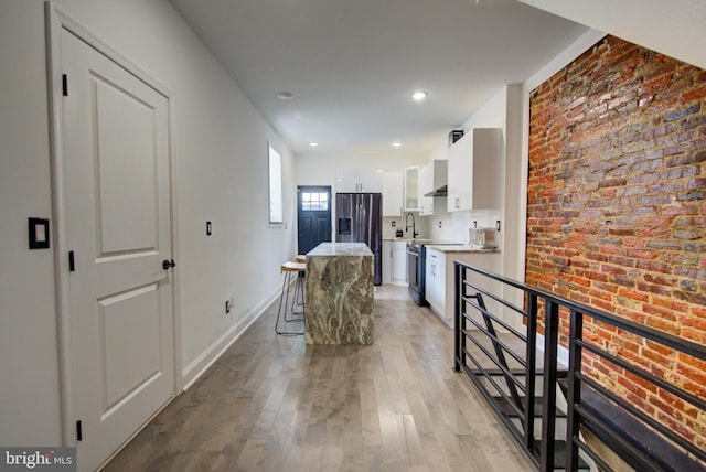 kitchen featuring a kitchen bar, white cabinetry, light hardwood / wood-style floors, brick wall, and stainless steel fridge with ice dispenser