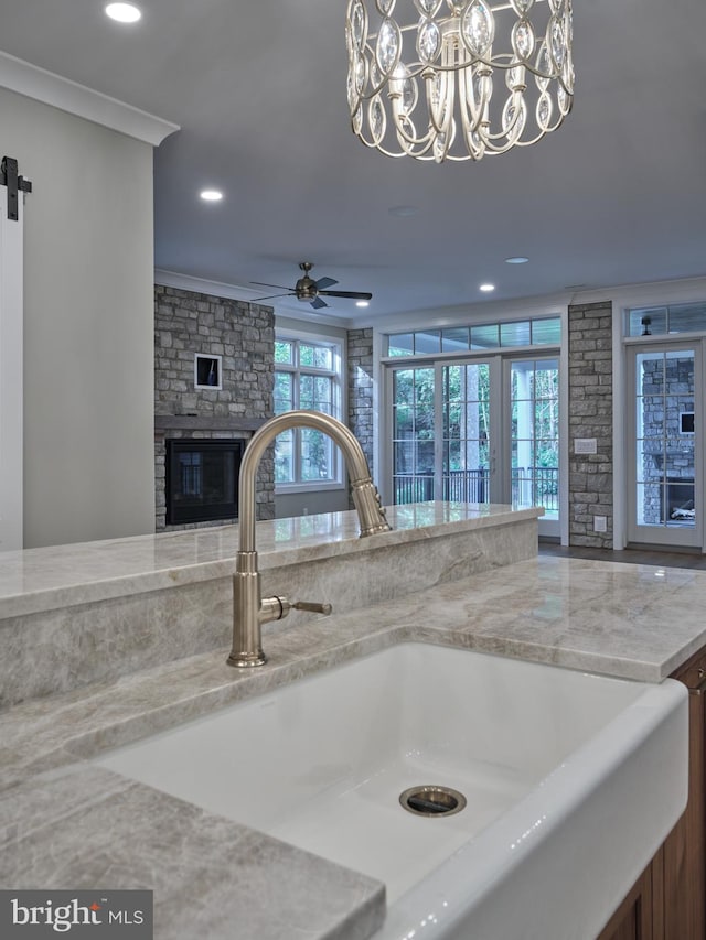 details featuring a stone fireplace, sink, crown molding, a barn door, and ceiling fan