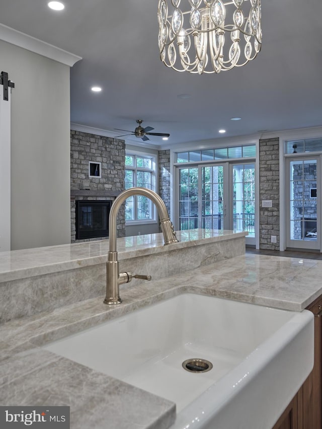interior details with a sink, a glass covered fireplace, pendant lighting, ornamental molding, and recessed lighting