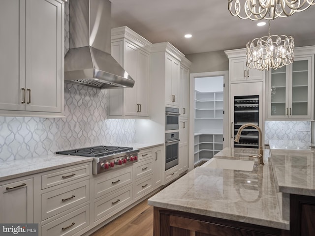 kitchen with wall chimney range hood, appliances with stainless steel finishes, backsplash, white cabinetry, and light hardwood / wood-style floors