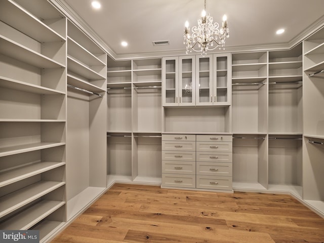 spacious closet with visible vents, light wood finished floors, and an inviting chandelier