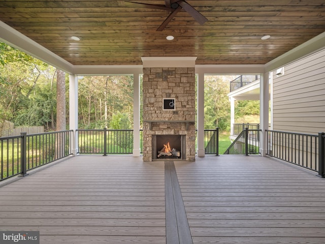 wooden terrace featuring fence, ceiling fan, and an outdoor stone fireplace