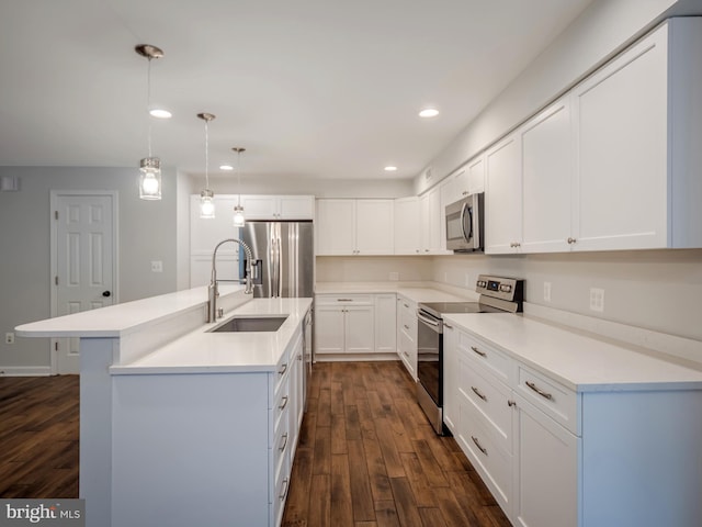 kitchen featuring appliances with stainless steel finishes, sink, white cabinets, hanging light fixtures, and a center island with sink