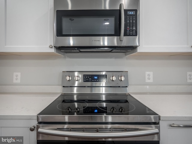 kitchen featuring stainless steel appliances, white cabinetry, and light stone counters