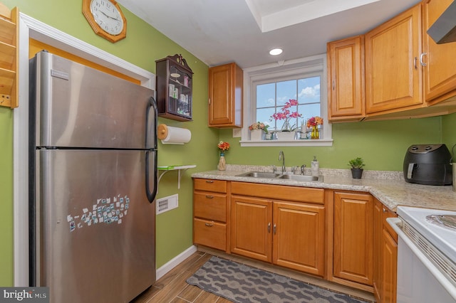 kitchen with white range, light hardwood / wood-style flooring, sink, stainless steel fridge, and light stone counters