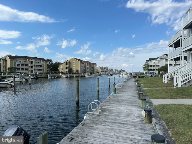 view of dock featuring a water view, a lawn, and a balcony