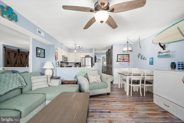 living room with a textured ceiling, a barn door, light wood-type flooring, and ceiling fan