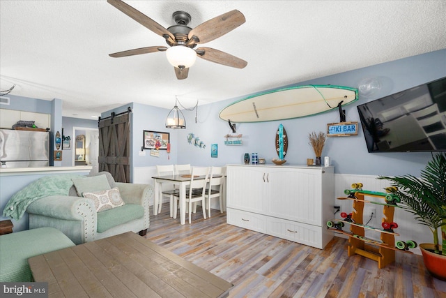 living room featuring a textured ceiling, a barn door, hardwood / wood-style flooring, and ceiling fan