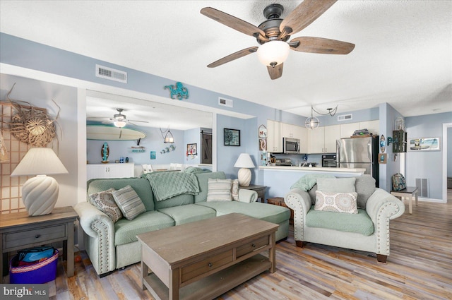 living room featuring light hardwood / wood-style floors, a textured ceiling, and ceiling fan