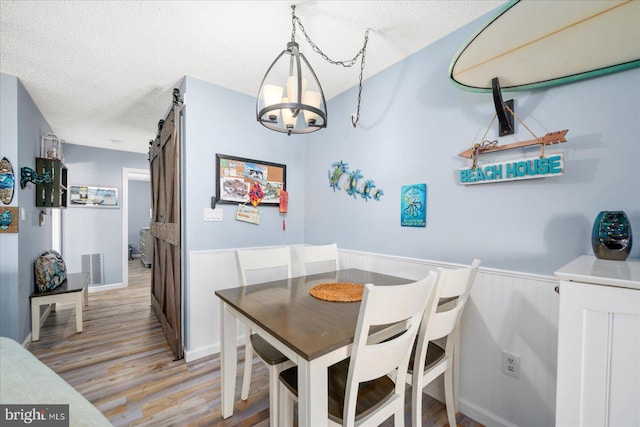 dining room with a chandelier, a barn door, a textured ceiling, and light wood-type flooring