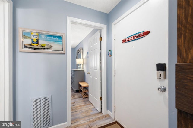 corridor with a textured ceiling and light hardwood / wood-style floors