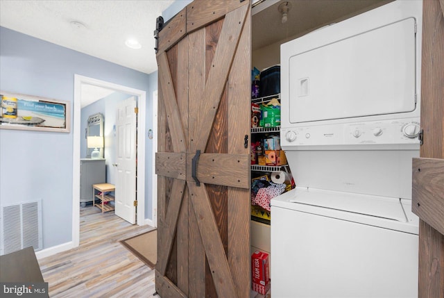 laundry room with stacked washer / drying machine, a barn door, and light wood-type flooring