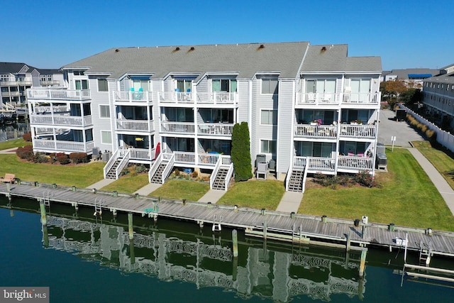 back of house with a balcony, a water view, and a lawn