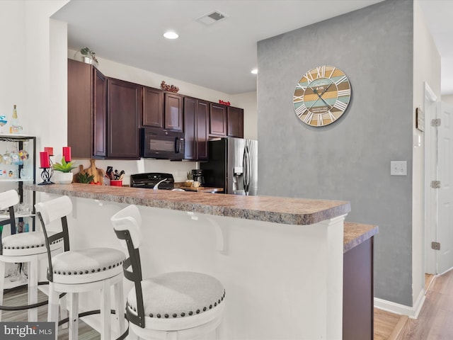 kitchen featuring a breakfast bar area, light hardwood / wood-style flooring, kitchen peninsula, black appliances, and dark brown cabinetry