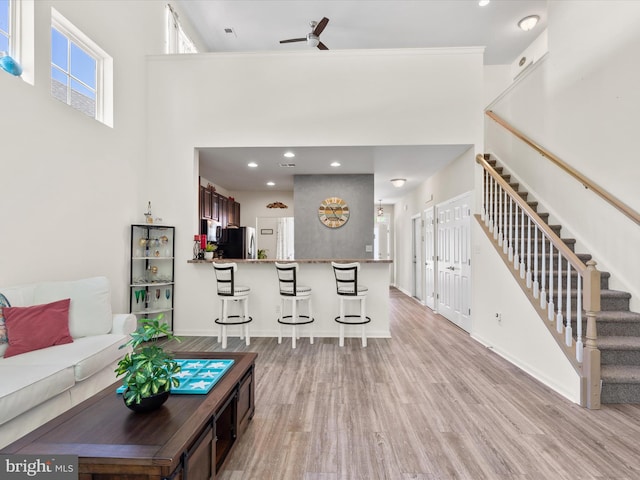 living room featuring ceiling fan, a towering ceiling, and light hardwood / wood-style flooring