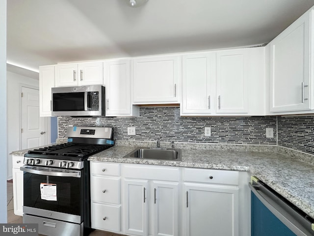 kitchen featuring appliances with stainless steel finishes, sink, light stone countertops, backsplash, and white cabinetry