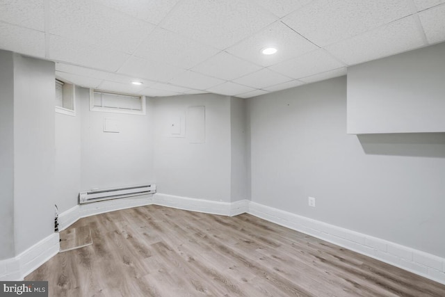 basement with a drop ceiling, a baseboard heating unit, and light wood-type flooring