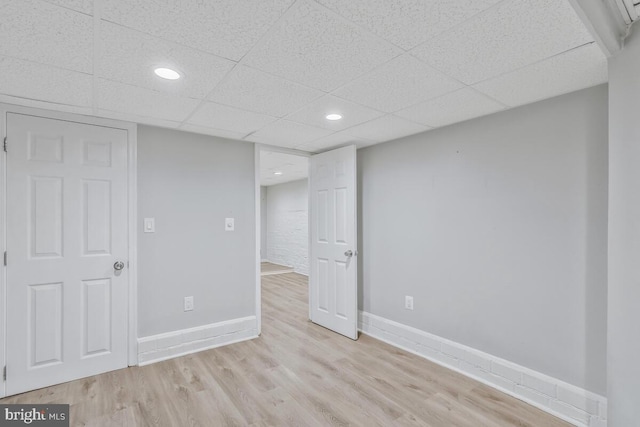 basement featuring a drop ceiling and light hardwood / wood-style flooring