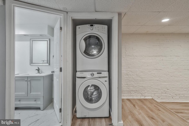 clothes washing area featuring sink, stacked washer and dryer, and light hardwood / wood-style flooring