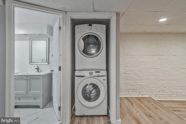 laundry area featuring brick wall, stacked washer / dryer, and a sink
