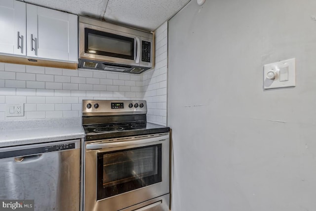 kitchen with decorative backsplash, white cabinetry, a drop ceiling, and stainless steel appliances