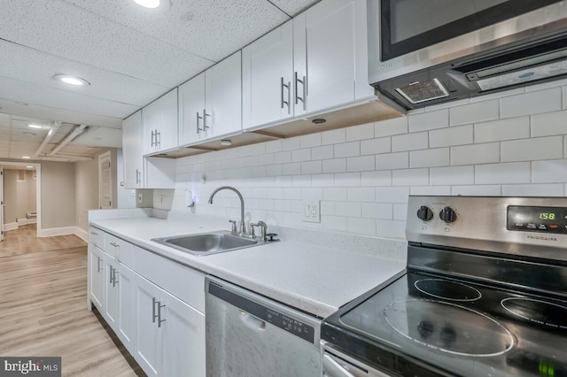 kitchen featuring white cabinets, a sink, backsplash, light countertops, and appliances with stainless steel finishes