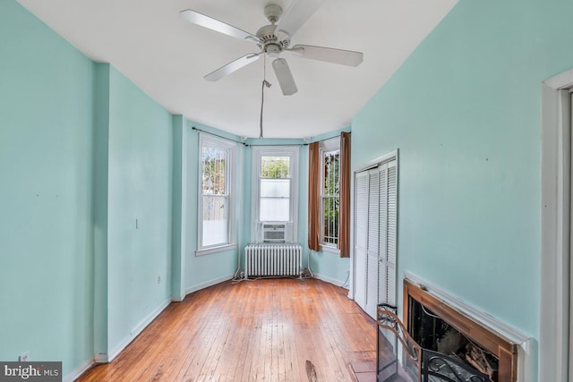 unfurnished room featuring a ceiling fan, hardwood / wood-style flooring, a fireplace, radiator, and baseboards