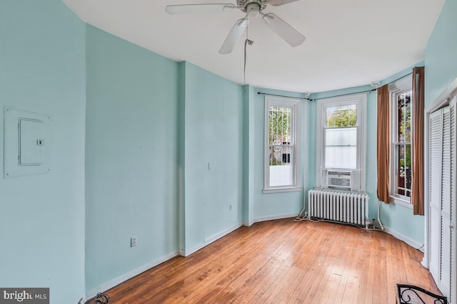 spare room featuring radiator heating unit, electric panel, light wood finished floors, and baseboards