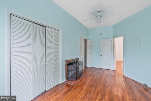unfurnished bedroom with ceiling fan, baseboards, hardwood / wood-style floors, and a fireplace with raised hearth